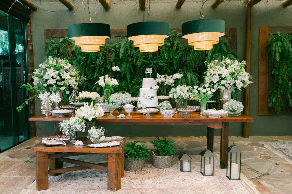 mesas rústicas com bolo de casamento com três andares e fotos instantaneas no topo e flores ao lado