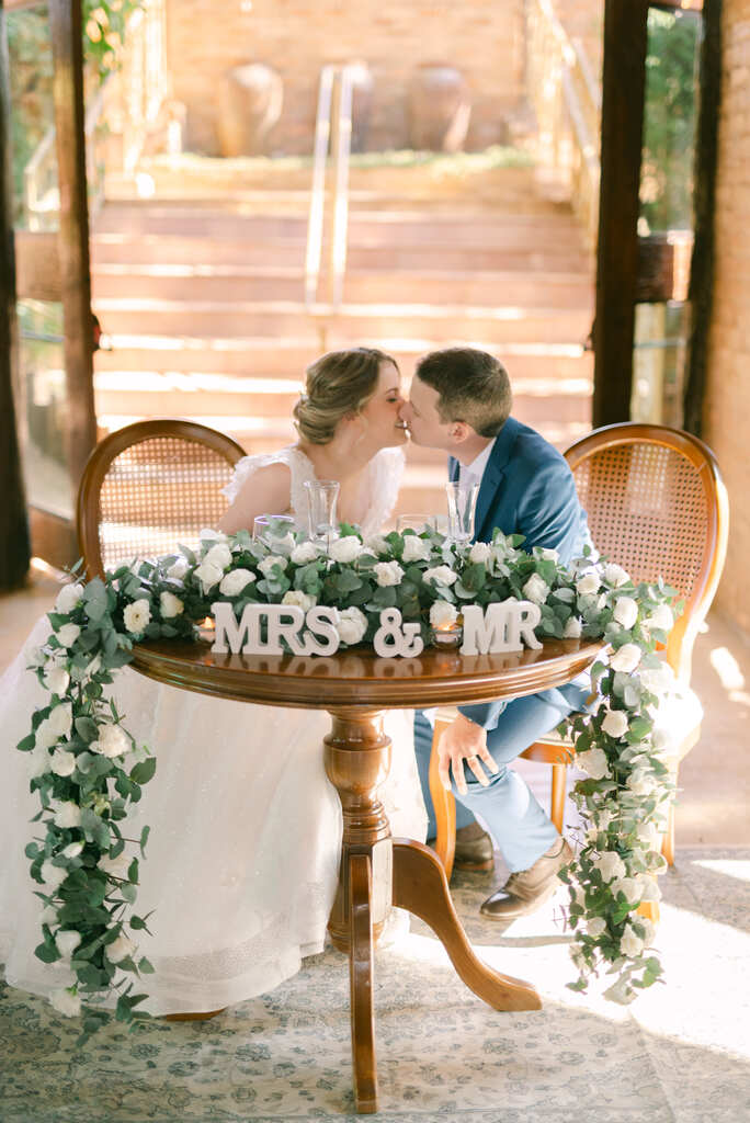 casal sentado na mesa dos noivos decorada com flores brancas