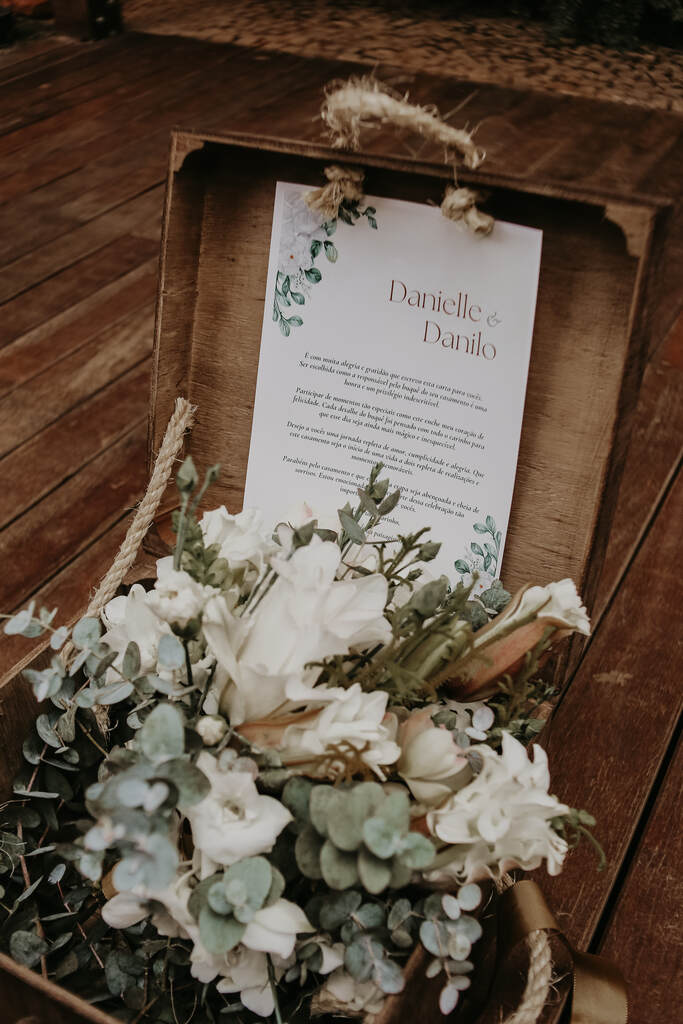 caixa rústica de madeira com carta dentro e ao lado buquê com flores brancas