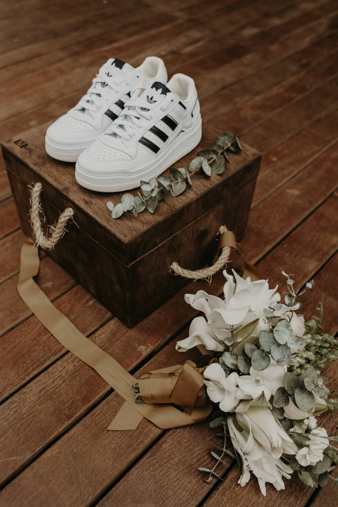 tênis adidas branco em cima de caixa rústica de madeira e ao lado buquê com flores brancas