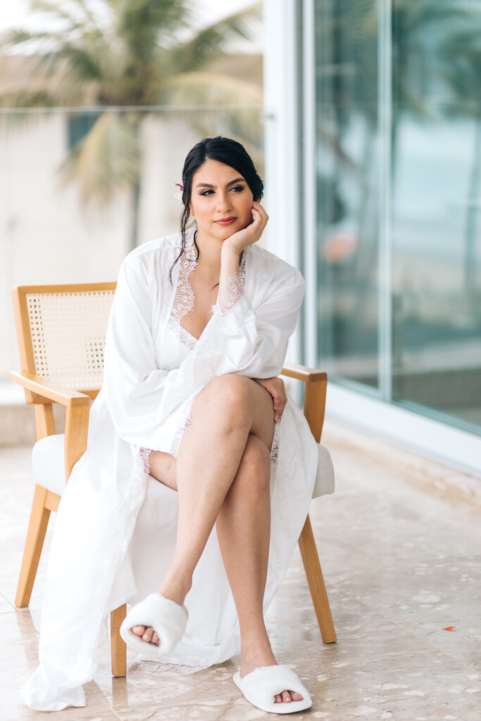 noiva com maquiagem leve e cabelo preso vestindo robe branco sentada na cadeira