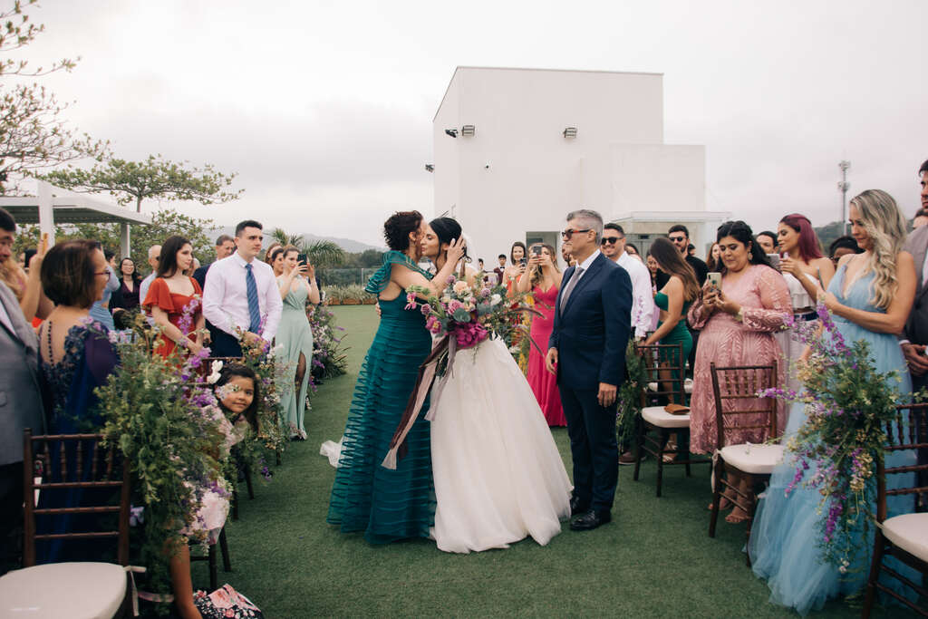 mãe da nova com vetsido verde beijando o rosto da noiva durnate a entrada na cerimônia