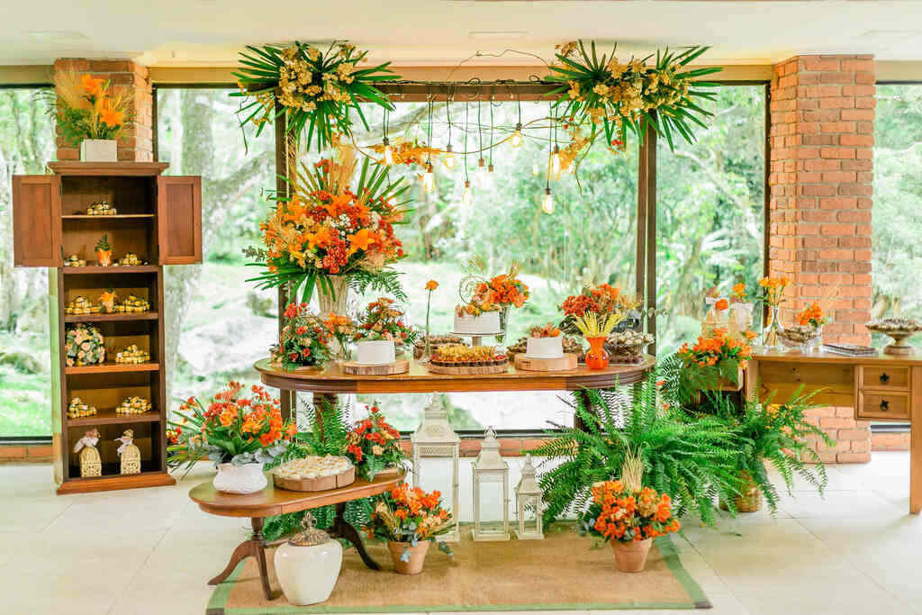 salão com mesa do bolo com vários arranjos com flores laranja