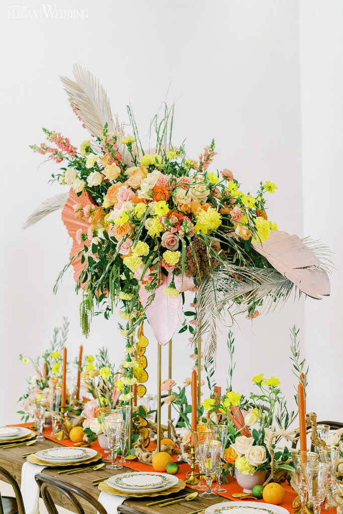 mesa posta com grande arranjo central com flores brancas laranjas e amarelas