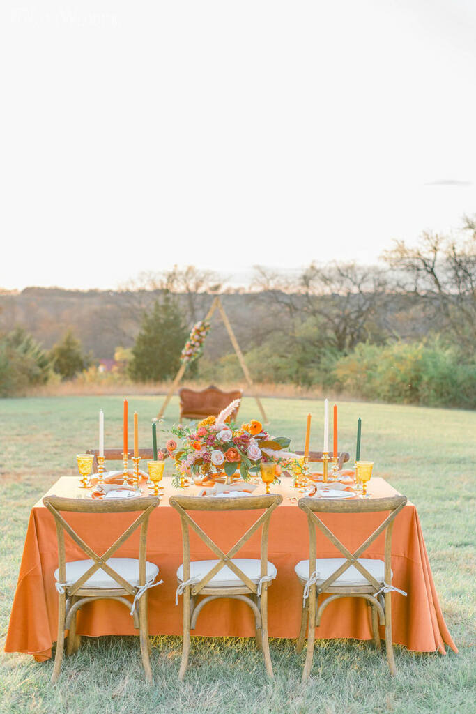 mesa comunitária com toalha laranja com mesa posta com velas e enfeites na cor verde e amarela