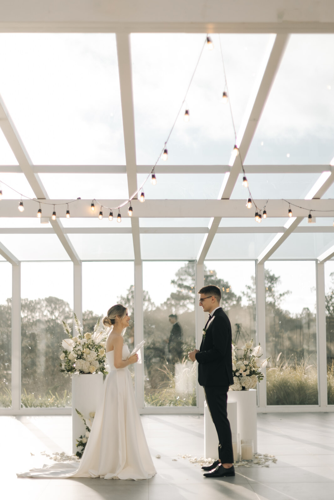 casal declarando os votos no altar dentro de salão branco minimalista com janelas e cobertura de vidro