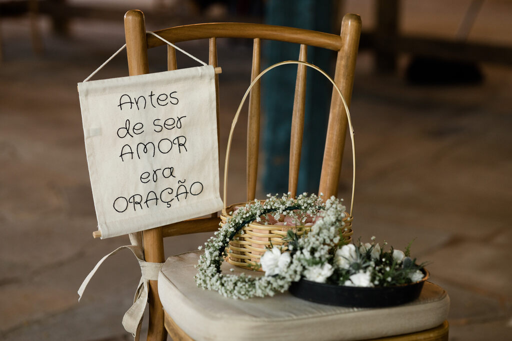 cadeira com coroa de flores brancas para madrinhas e plaquinha bordado antes de ser amor era oração