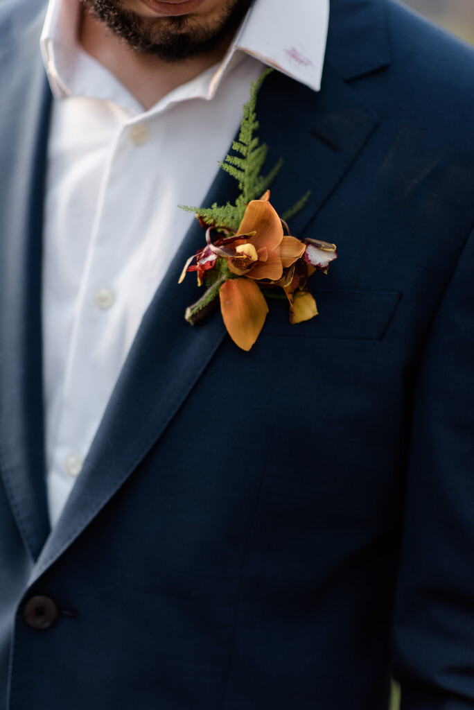 close no noivo com terno mostrando flor de lapela laranja
