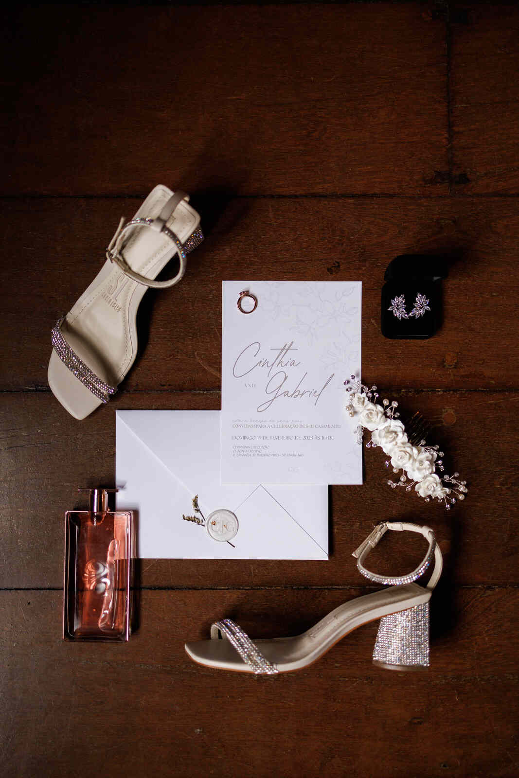 convite de casamento minimalista ao lado de grinalda floal brinco vidro de perfume vermelho e sapato da noiva com aplique de strass