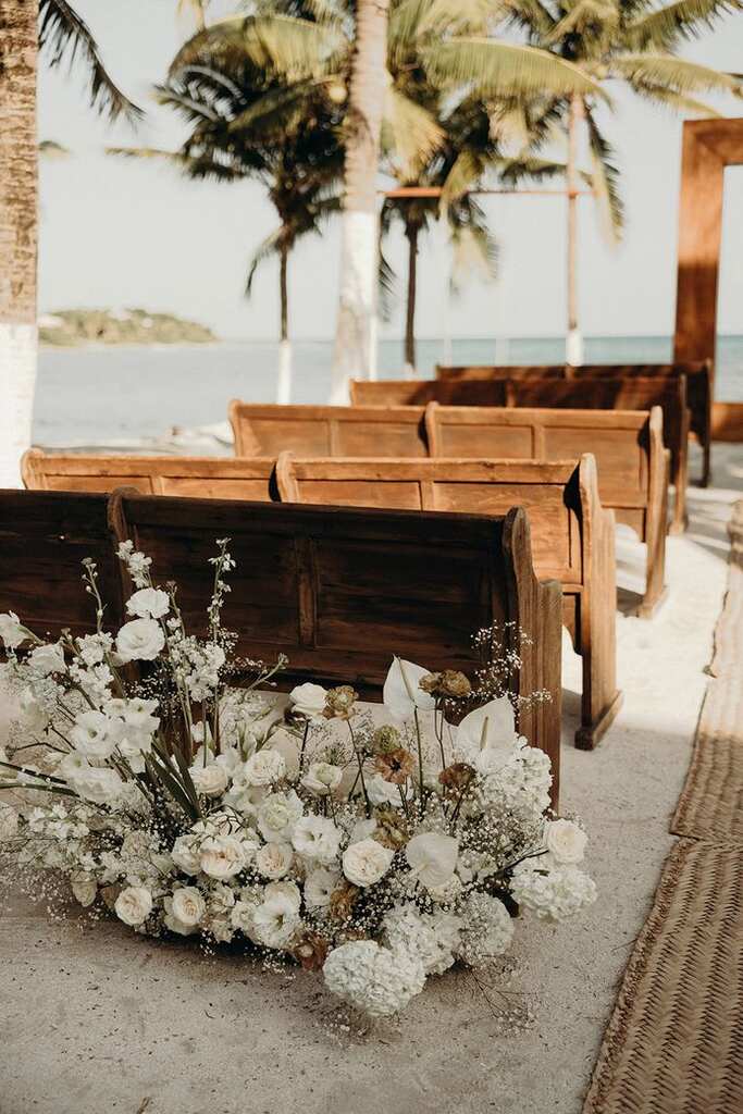 bancos de madeira na praia com arranjos de flores brancas