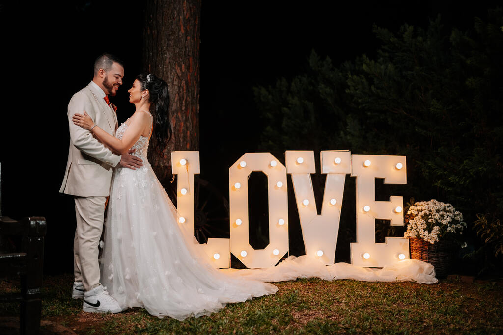 noivos abraçados ao lado de letreiro iluminado escrito love
