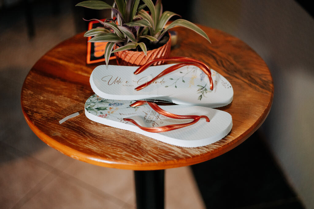 chinelo branco personalizado em cima de mesa de madeira ao lado de vasinho com plantas