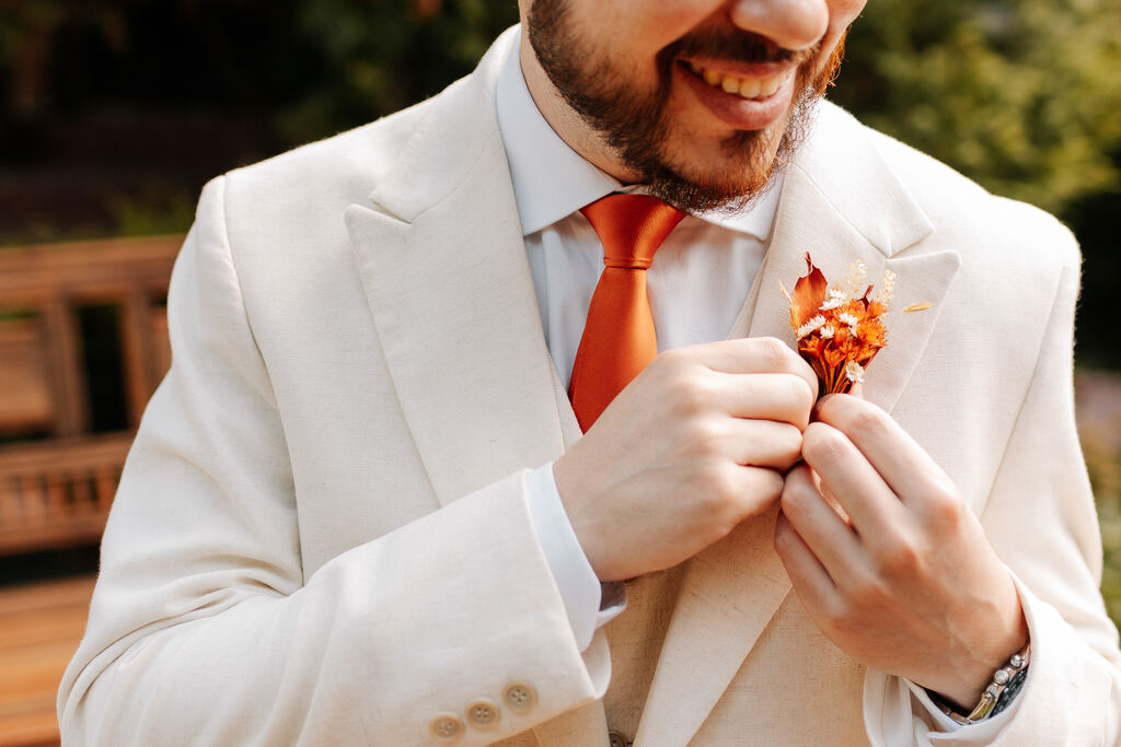noivo com terno off white com gravata e flor de lapela laranja