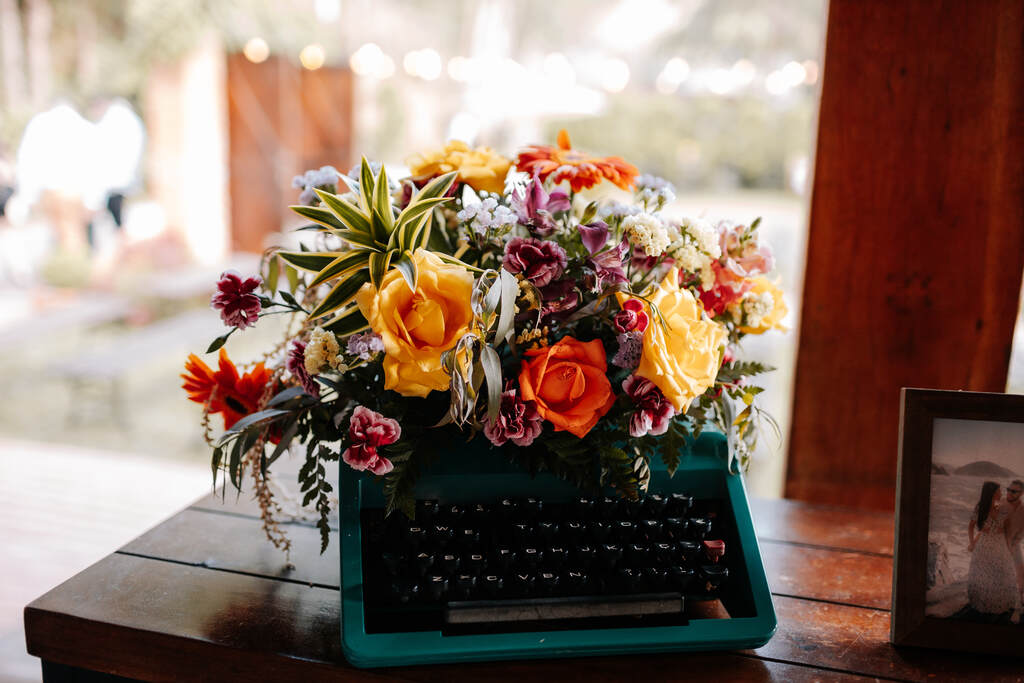 maquina de escrever azul com flores vermelhas e amarelas e plantas em cima