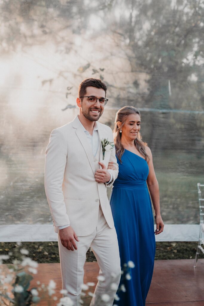 entrada do noivo com tenro off white ao lado da mãe com vetsido azul de ombro único
