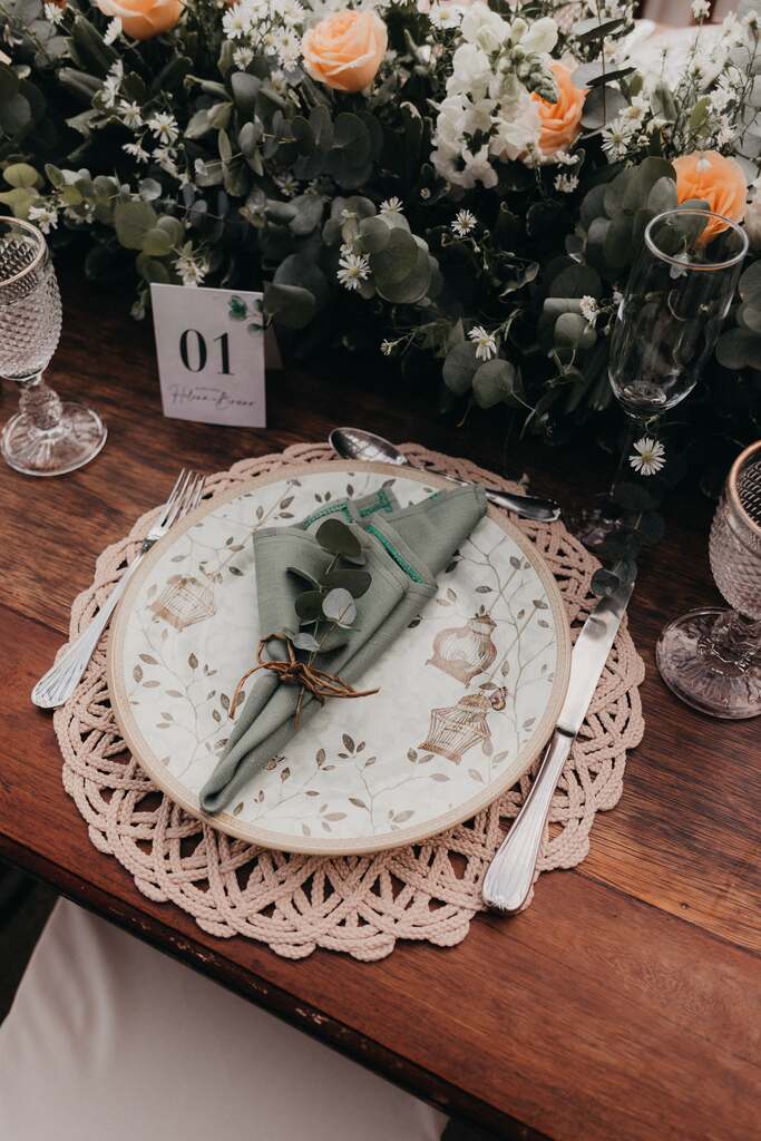 mesa posta com sousplat trabalhado e prato estampada com guardanapo verde cintilante amarrado com ramo de eucalipto