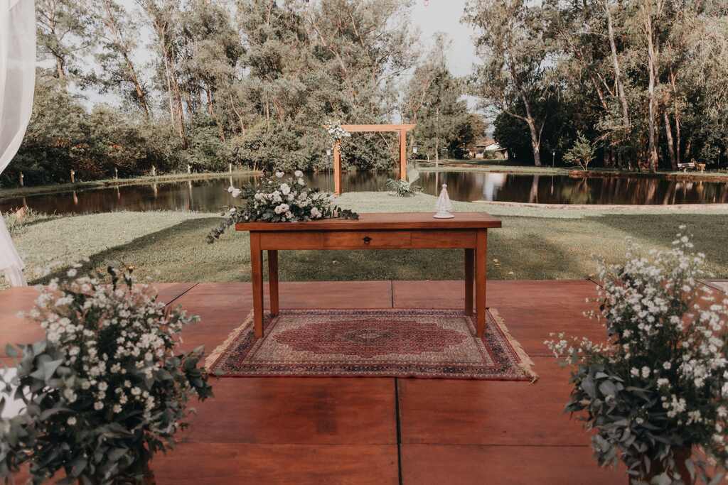 altar rústico com mesa de madeira e tapete etnico antigo e ao lado arranjos com flroes brancas e ramo de eucaliptos
