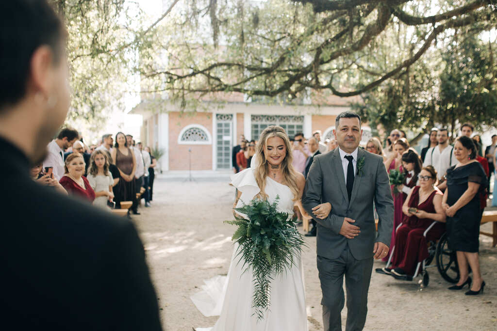 Entrada da noiva com buquê de folhagens greenery ao lado do padrasto com tenro cinza médio e gravata preta