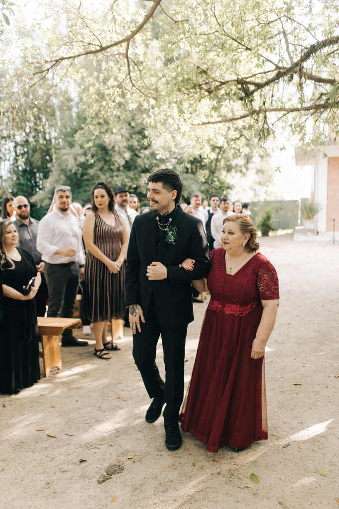 entrada do noivo com terno all black ao lado da mãe com vestido longo e decote em v na cor vinho