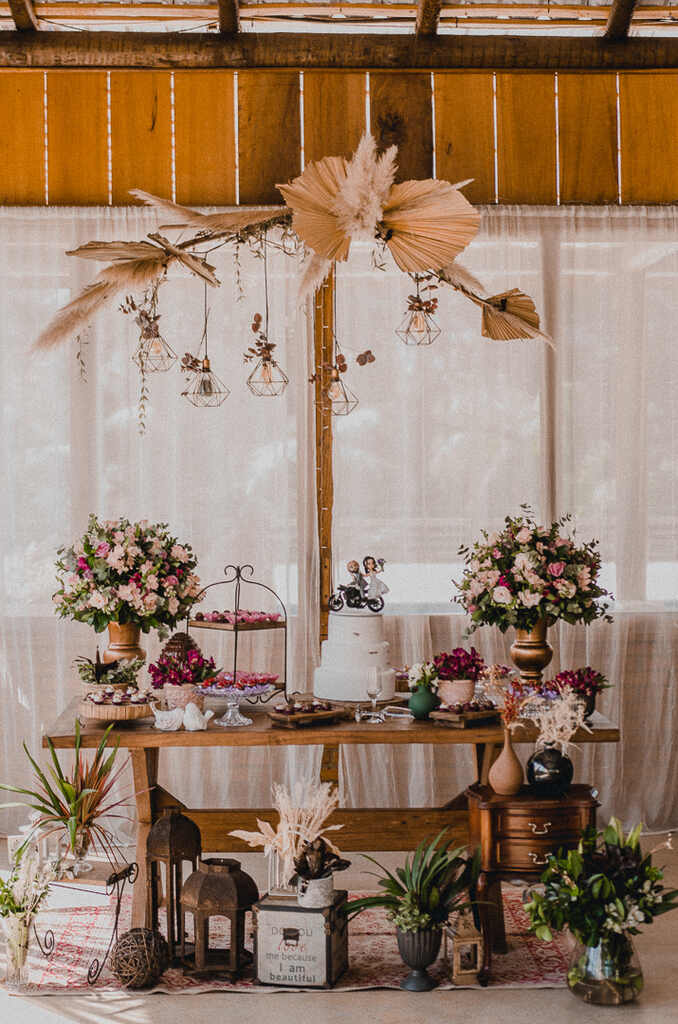 mesa de madeira com bolo de casamento e ao lado bandejas com doces e vasos com flroes
