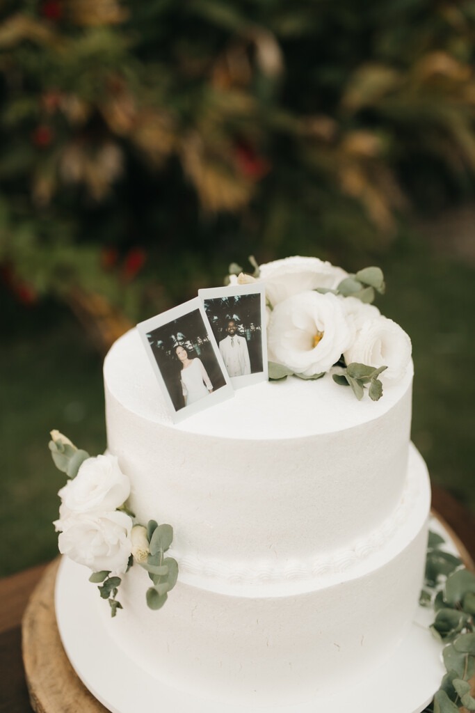 bolo de casamento minimalista branco com folhas de eucalipto e fotos polaroide no topo