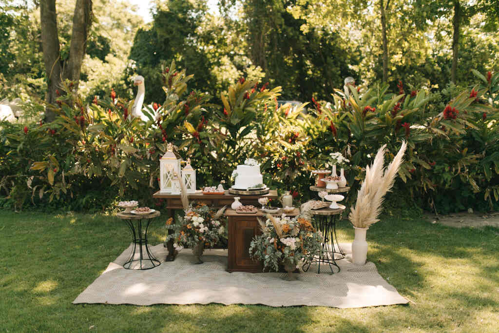 tapete bege no campo mesas de madeira rústicas decoradas com flores pequenos vasos e bolo de casamento