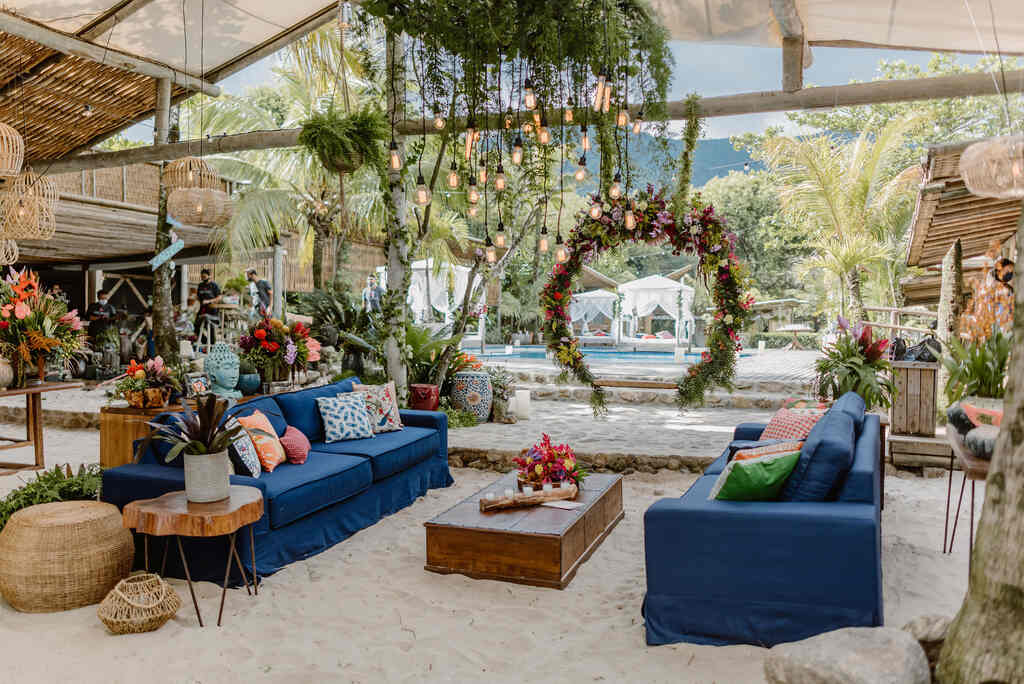 decoração de casamento na praia com sofás azuis almofadas estampadas e coloridas e arranjo pendente com luminaria