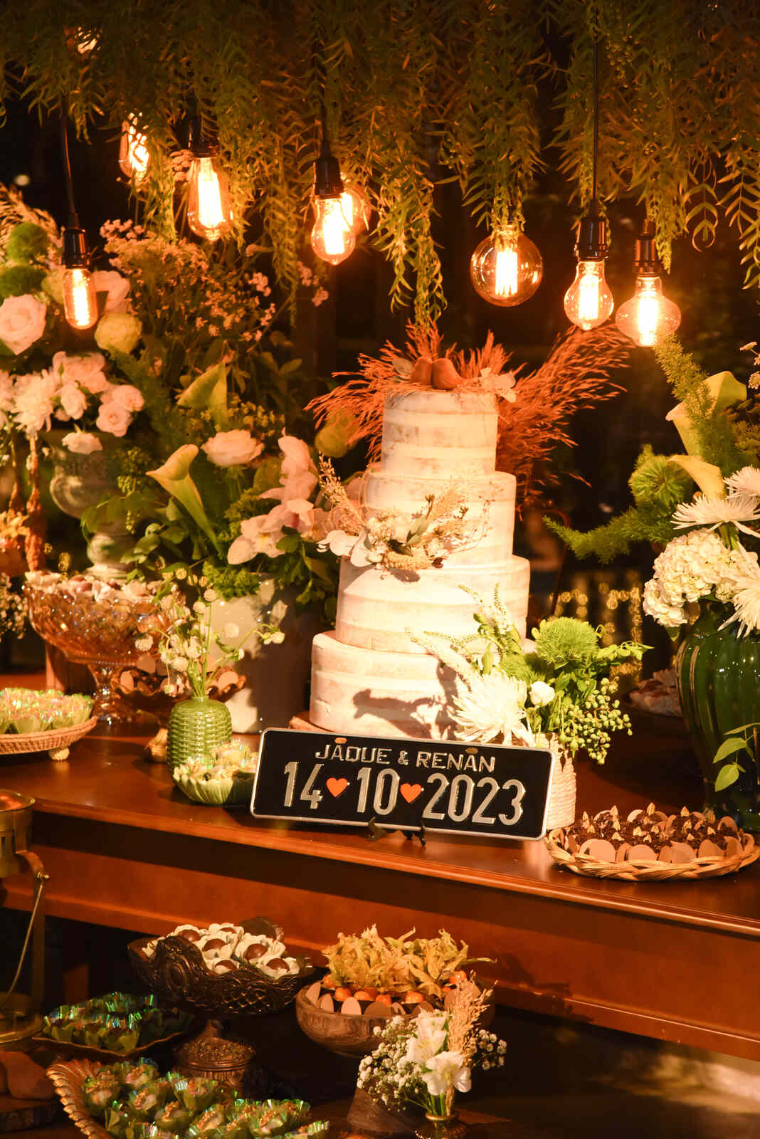 mesa com bolo de casamento com quatro andares com flores no topo