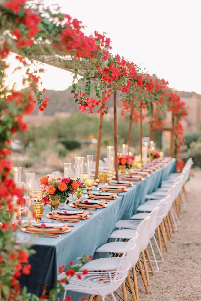 decoração de casamento na praia com mesa comunitária com toalha azul e flores pendentes vermelhas