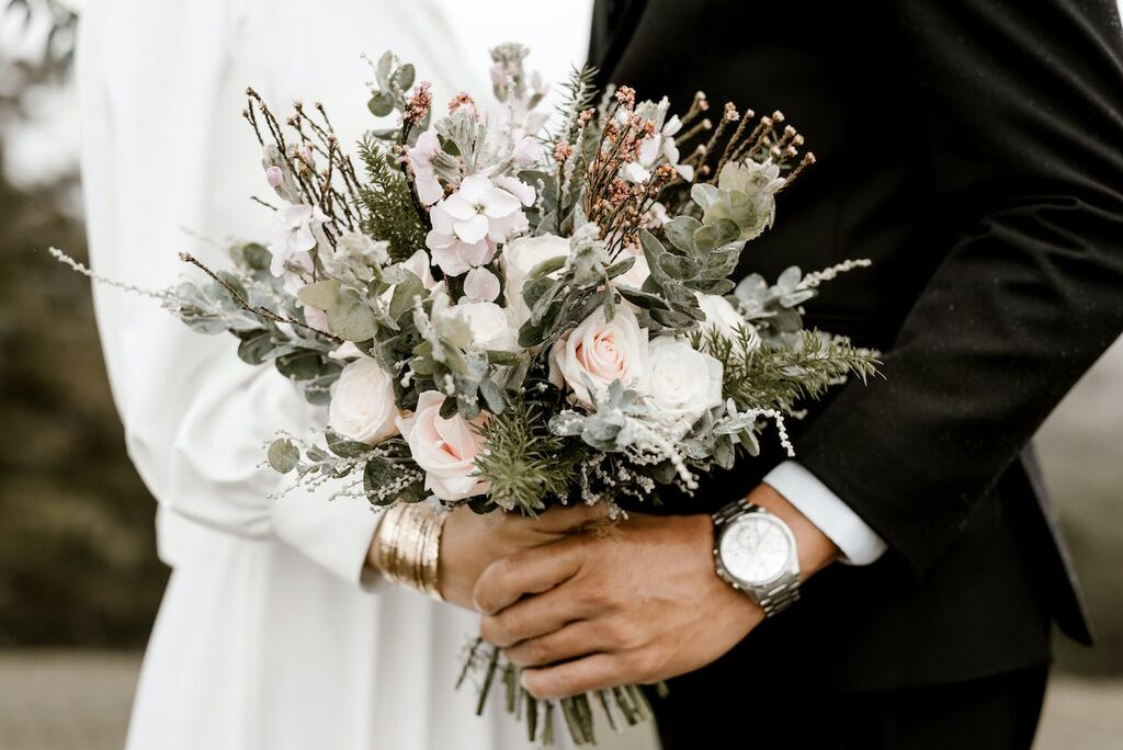 casal de mãos dadas segurando buquê com rosas brancas e cor de rosa