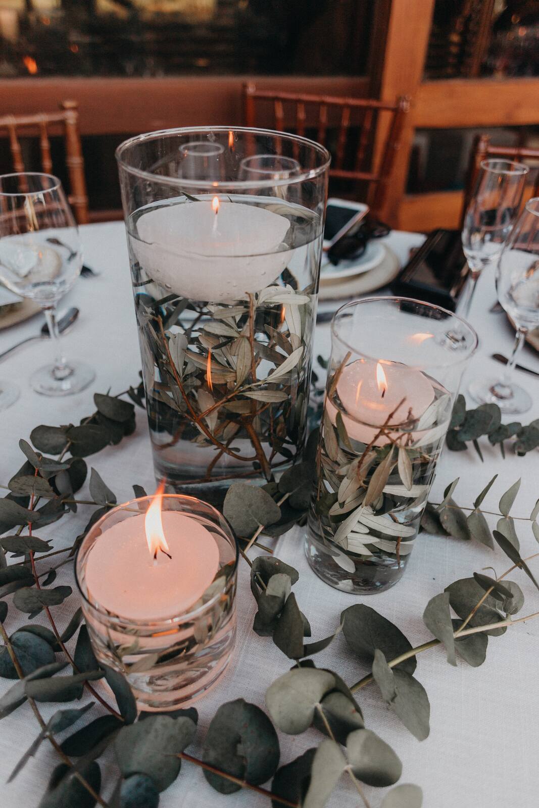 centro de mesa com vasos de vidro decorados com velas brancas na água com ramos de eucalipto
