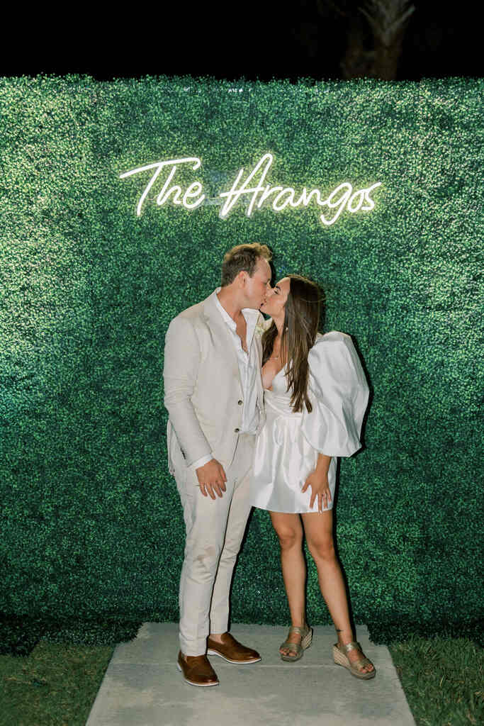 casal se beijando na frente de backdrop com folhagens e painel luminoso