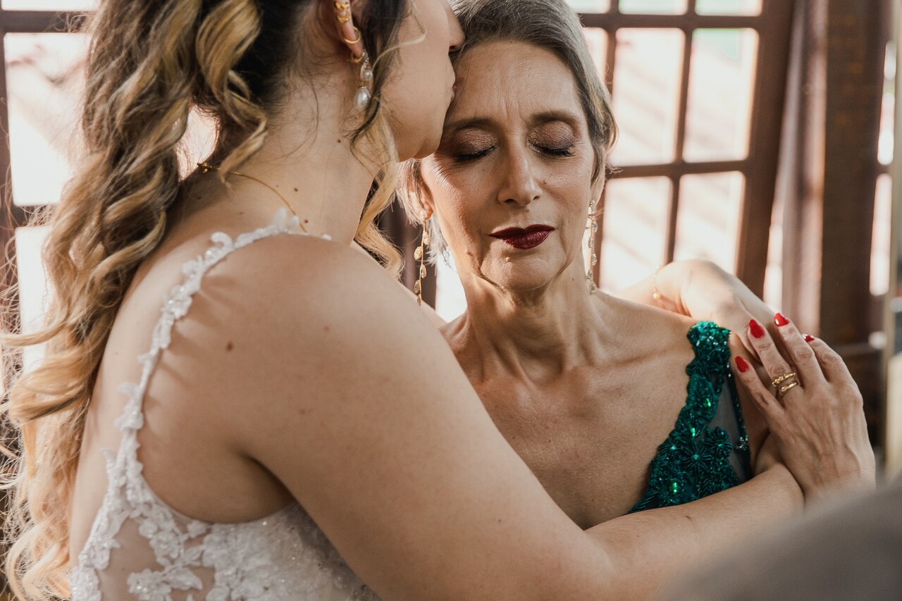 noiva beijando a testa da mãe usando vetsid verde escuro e com batom marsala