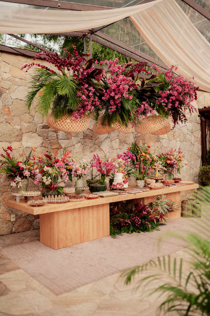 mesa de madeira com bolo de casamento com flores cor de rosa ao lado de vasos com flores rosas brancas e vermelhas