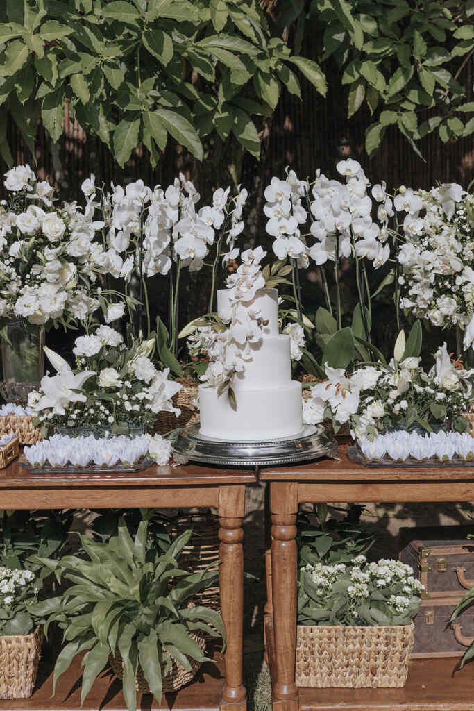 mesa de madeira ao ar livre com vasos com orquideas brancas e bolo decorado com flores