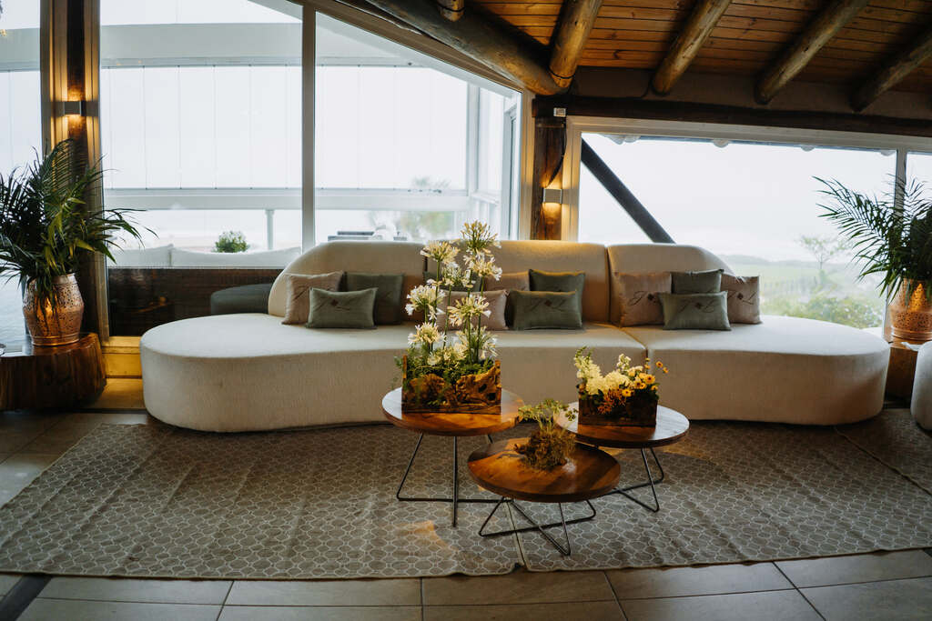 lounge com sogfá branco curvo com almofadas verdes e cinzas e jogo de mesa de centro 