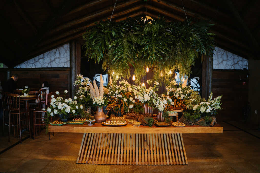 mesa com doces de casamento folhagens aéreas e flores brancas