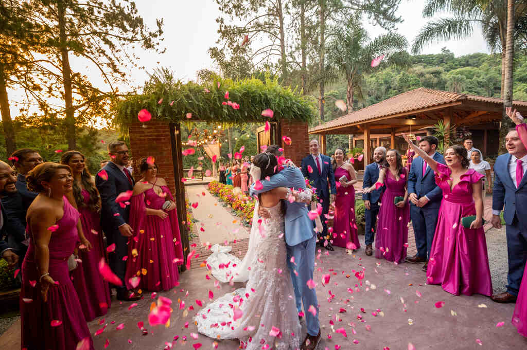 novios se beijando sob pétalas cor de rosa na saída em volta dos padrinhos e madrinhas