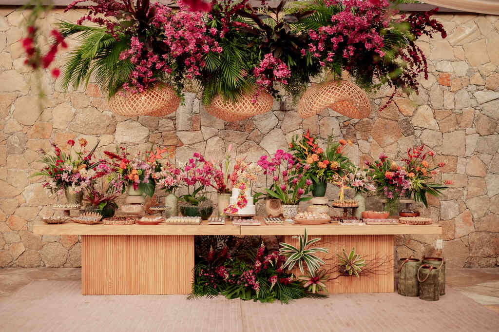 mesa de madeira com bolo de casamento com flores cor de rosa ao lado de vasos com flores rosas brancas e vermelhas