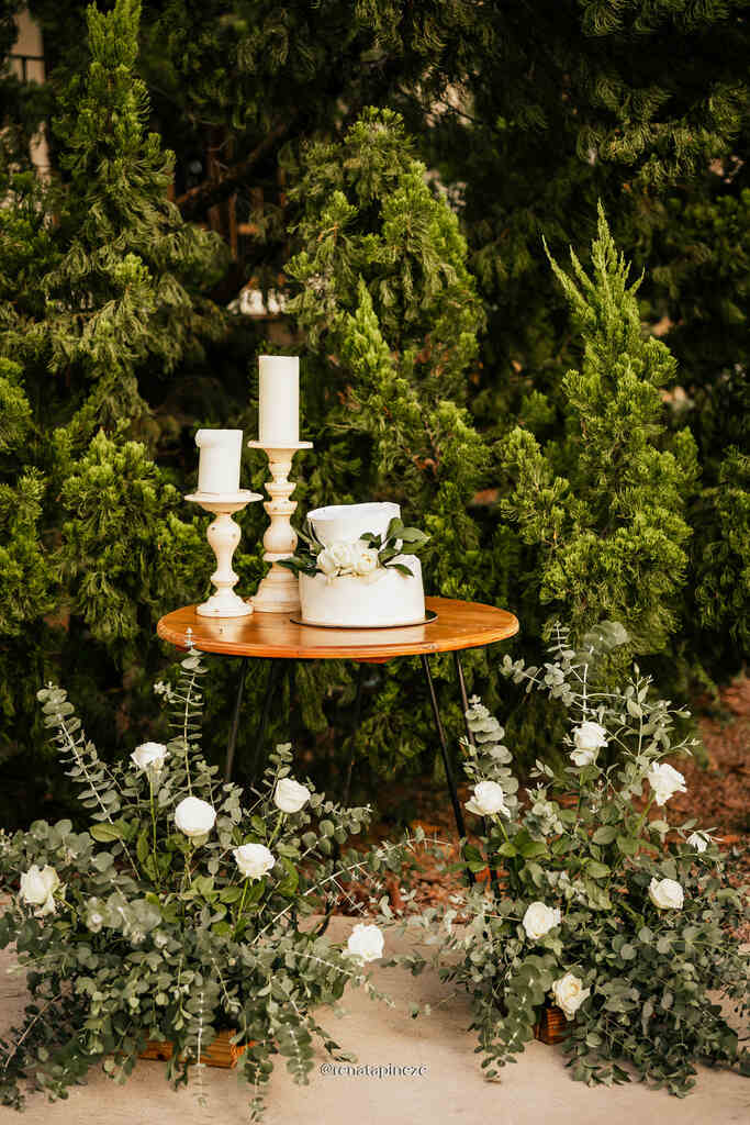 mesa de madeira redonda pequena com bolo de casamento e castiçais com velas brancas