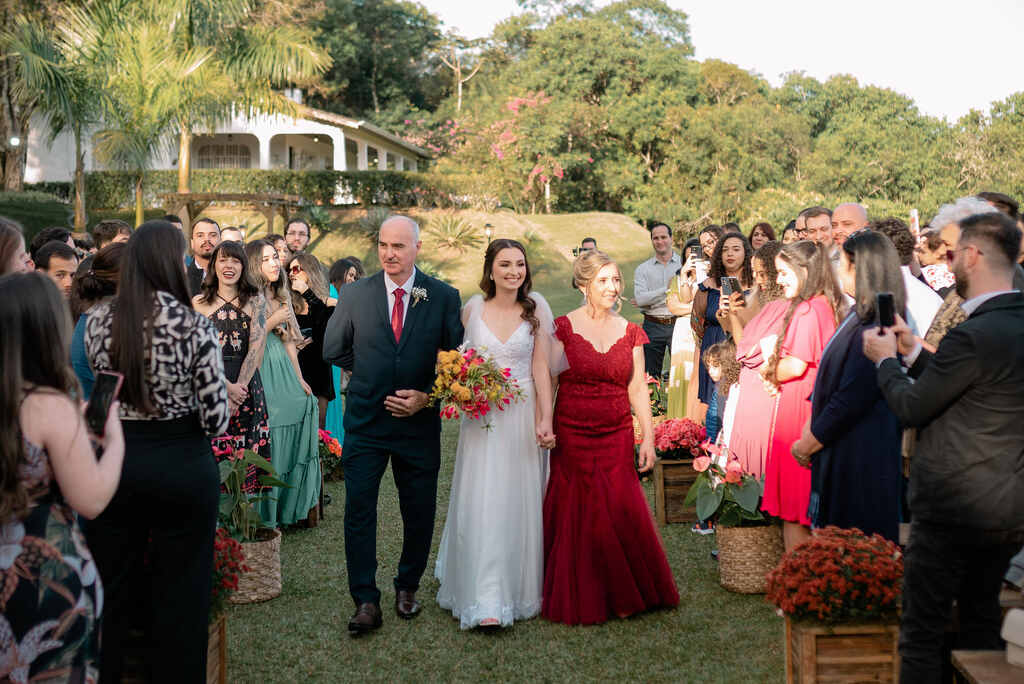entrada da noiva com pai com terno preto e garvata vermelha ao lado da mãe com vestido vermelho longo semi sereia