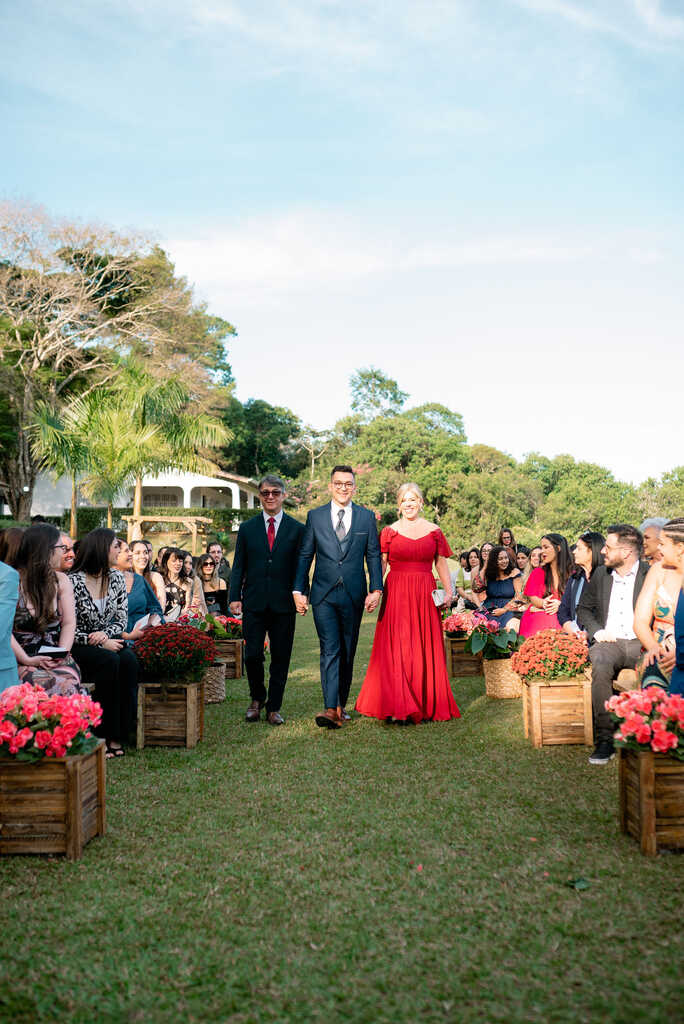entrada do noivo com terno azul ao lado do pai com terno preto e mãe com vestido vermelho