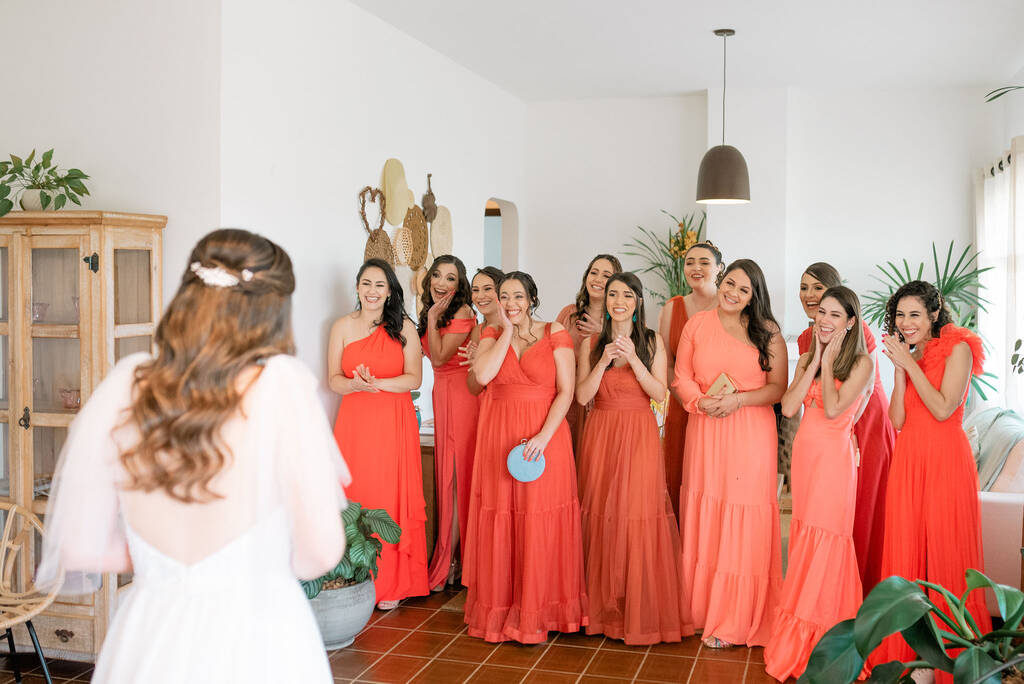 11 madrinhas com vestidos longos na cor laranja reagindo ao ver a noiva pela primeira vez