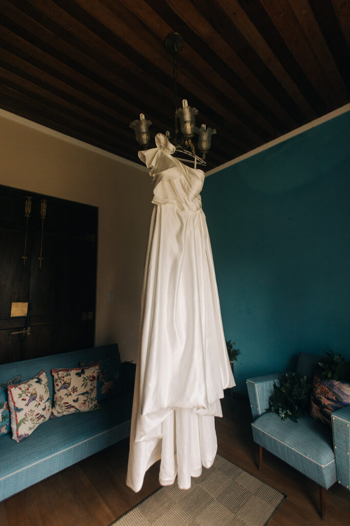 vestido de noiva com ombro único com babados pendurado no meio de sala