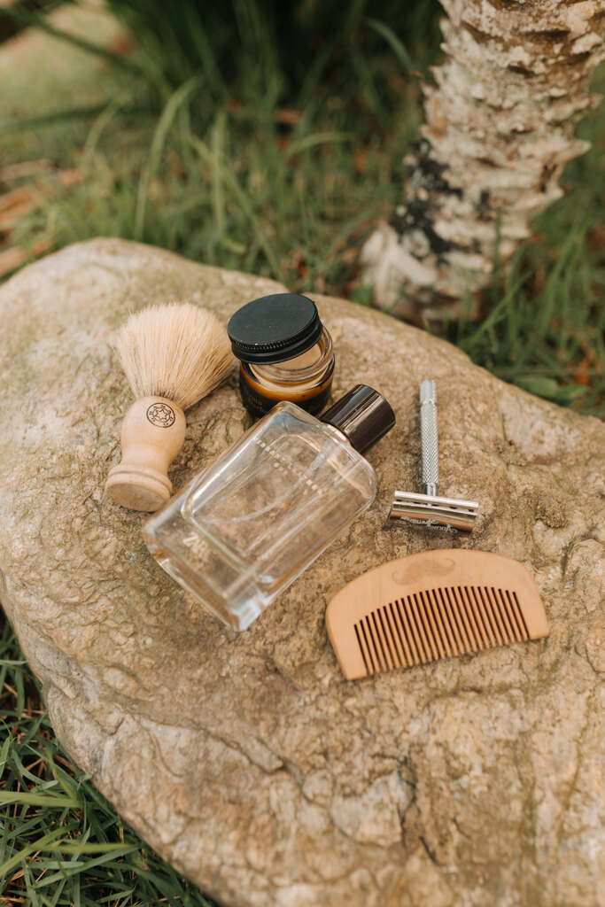 frasco de perfume barbeador de ferro e pente de madeira masculino em cima de pedra