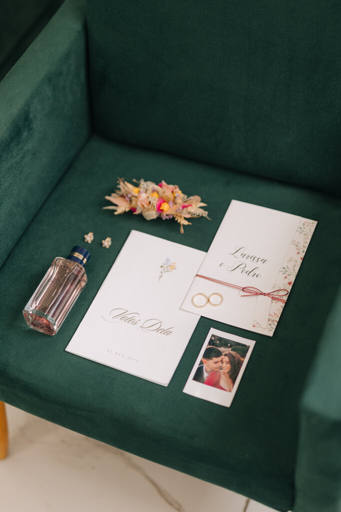 papelaria de casamento ao lado de foto instantanea frasoc de perfume e grinalda floral sobre poltrona verde