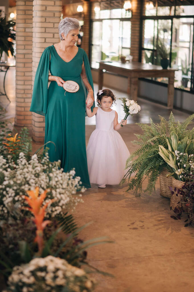 entrada da mãe levando porta aliança bordado com vestido verde de mãos dadas com a daminha carregando buquÊ branco