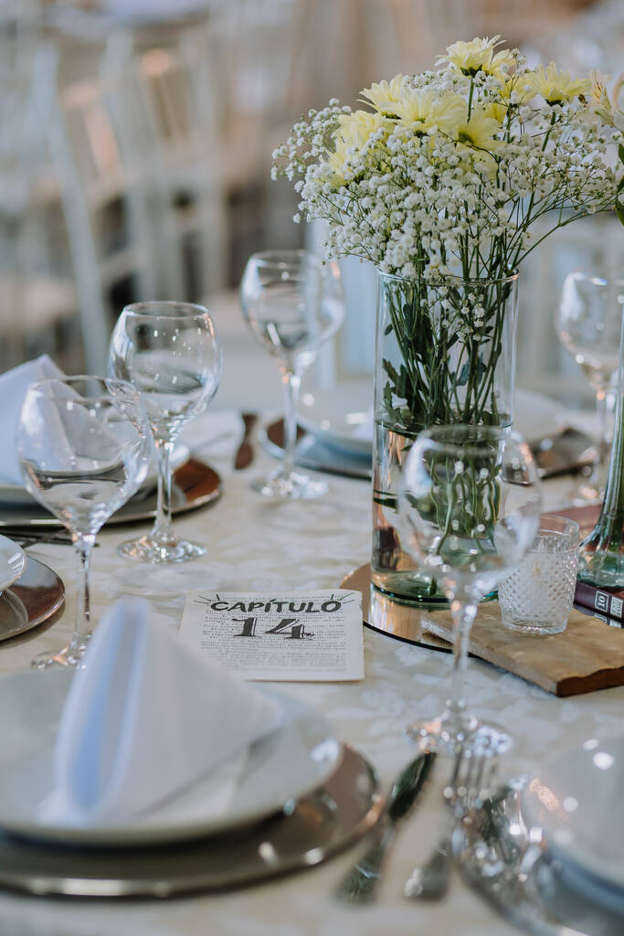 mesa posta elegante com vaso de vidro com flores brancas no centro e marcador de mesa em págian de livro
