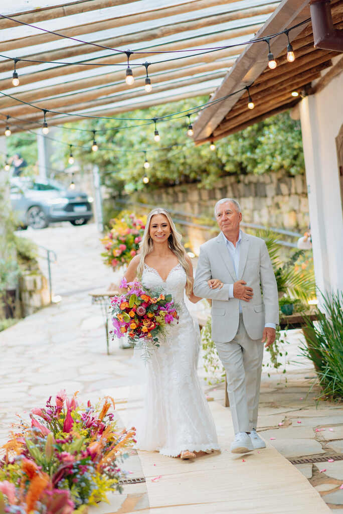 entrada da noiva com buquê com flores coloridas ao aldo do pai com terno cinza