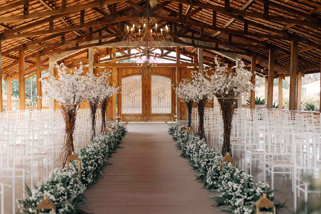 salão rústico de madeira com caminho das noivas com flores brancas e cadeiras tiffany